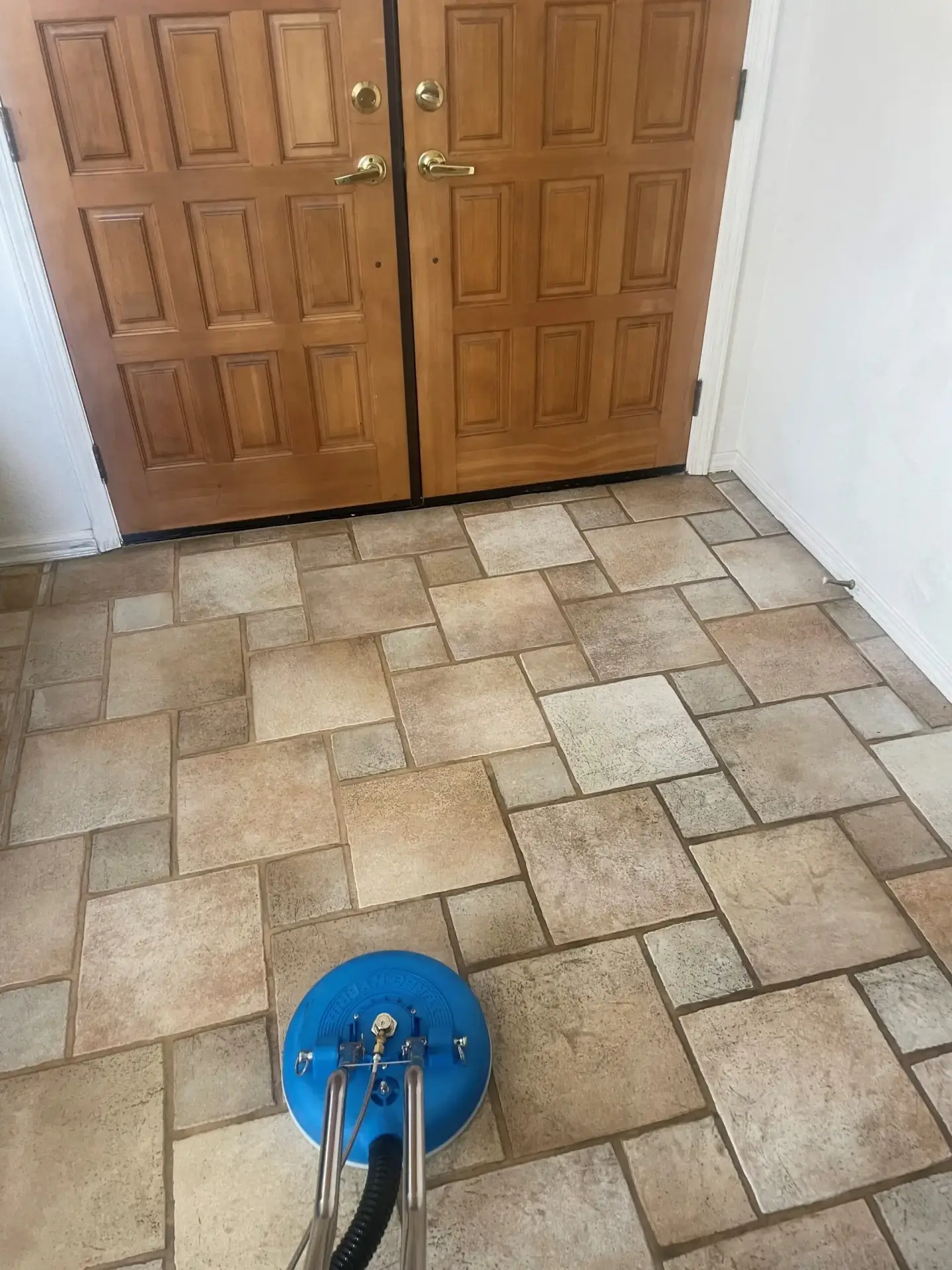 Tile and grout floor cleaning with professional machine near wooden door